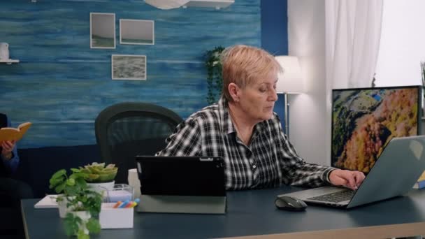 Stará manažerka psaní na notebook a čtení na tablet ve stejnou dobu — Stock video