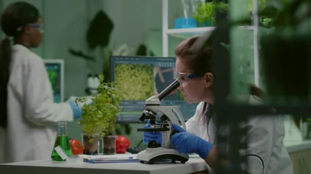Pharmawissenschaftler betrachtet grüne Blattprobe unter dem Mikroskop — Stockvideo