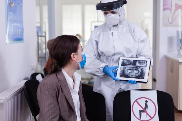 Stomatologist in protective suit pointing on digital x-ray of tooth
