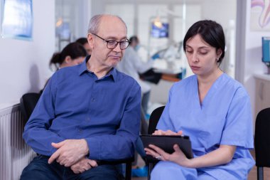 Hemşire, dişçi muayenehanesindeki kıdemli hastayla tartıştığı tablet hakkında notlar alıyor.