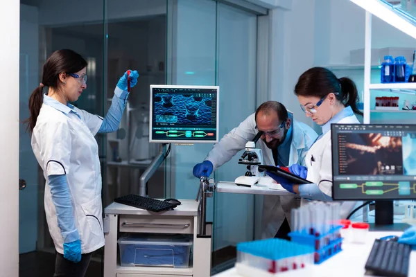 Scientist analyzing blood sample in vacutainer with researching team — Stock Photo, Image
