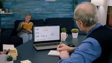 Yorgun yaşlı girişimci dizüstü bilgisayardaki grafikleri kontrol ediyor.