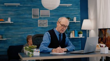 Dizüstü bilgisayarda okuyan ve deftere yazan çok görevli emekli adam