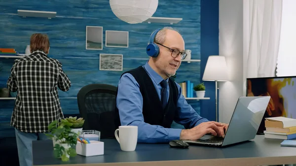 Vieil homme âgé écoutant de la musique sur un casque tout en travaillant sur un ordinateur portable — Photo