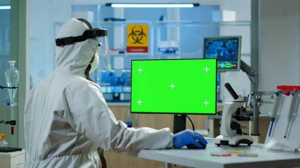 Naukowiec noszący kombinezon ochronny na komputerze z zieloną makietą — Zdjęcie stockowe