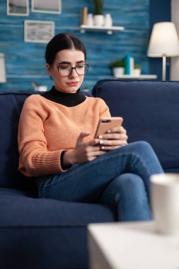 Öğrenci mesaj yazarken oturma odasında kanepede rahat yatıyor.