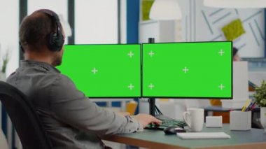 Kulaklıklı bir çalışan yeşil ekranlı çift ekran monitörde çalışıyor.