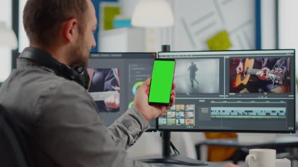 Editor de vídeo hablando en videollamada sosteniendo smartphone con pantalla verde — Vídeos de Stock