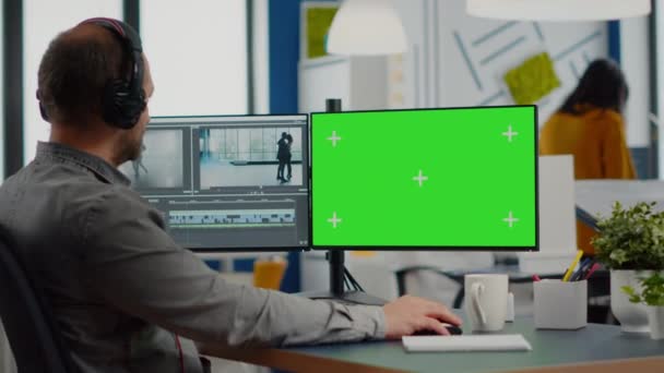 Hombre videógrafo con auriculares trabajando en el ordenador de pantalla verde — Vídeos de Stock