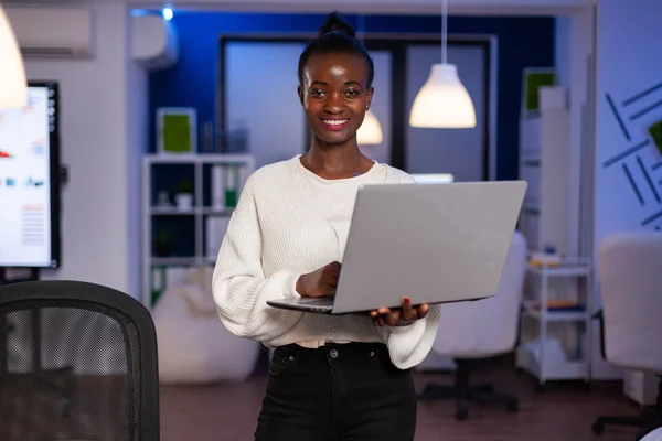 Siyah iş kadını elinde dizüstü bilgisayarla kameraya bakıp gülümsüyor. — Stok fotoğraf