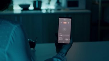 Otomasyon ışığı sistemi olan evde oturan bir kadın akıllı telefon tutuyor.