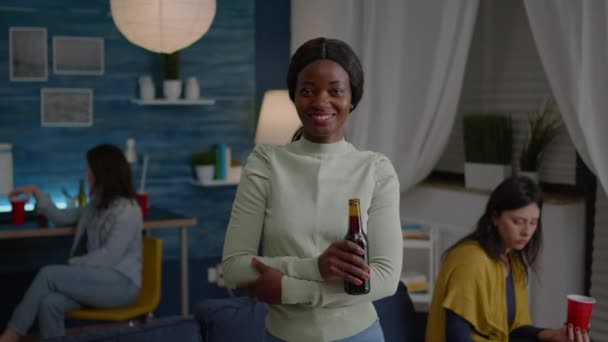 Potrait de mujer afroamericana sonriendo a la cámara mientras sostiene la botella de cerveza — Vídeos de Stock