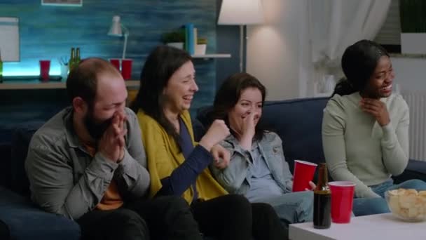 Мультирасовая команда смотрит комедийные фильмы, сидя на диване — стоковое видео