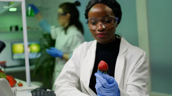 Químico africano con gafas médicas mirando fresa inyectada con pesticidas químicos — Foto de Stock