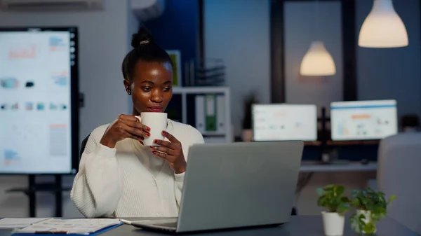 Nero donna d'affari utilizzando cuffie bere caffè duing video conferenza — Foto Stock
