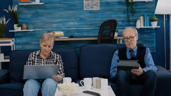 Senior man probeert op tablet, terwijl zijn vrouw maakt gebruik van laptop — Stockfoto