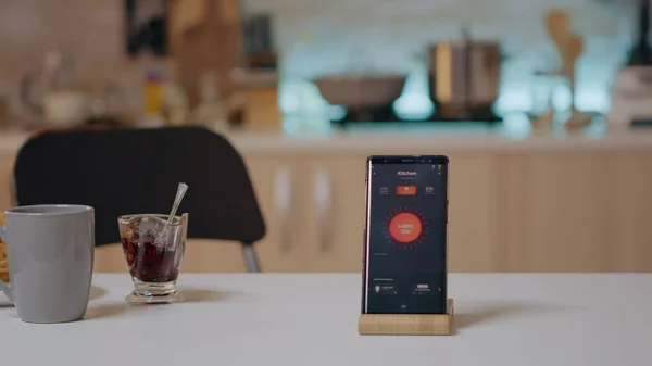 Smart home application on phone placed on kitchen desk in empty house