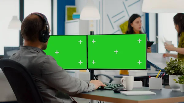 Empleado con auriculares que trabajan en configuración de monitor dual con pantalla verde — Foto de Stock