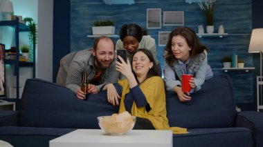 Karışık ırk arkadaşları gece partisinde dinlenirken online film izliyorlar.