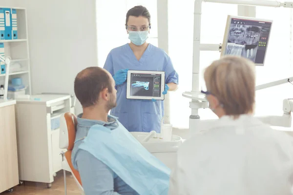 Assistente medico che esamina la radiografia dei denti al paziente malato — Foto Stock