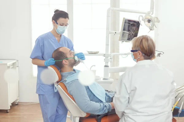 歯科手術のための病気の男性患者を調べる酸素マスクを置く医療アシスタント — ストック写真