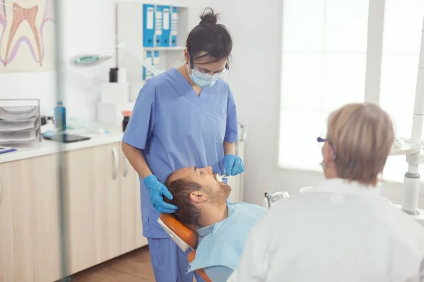 Medische assistent vrouw doet tandheelkundige behandeling aan zieke man — Stockfoto