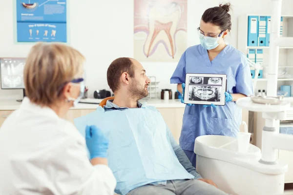 Больной человек сидит на стоматологическом чайнике и смотрит на рентгенографию на цифровом планшете — стоковое фото