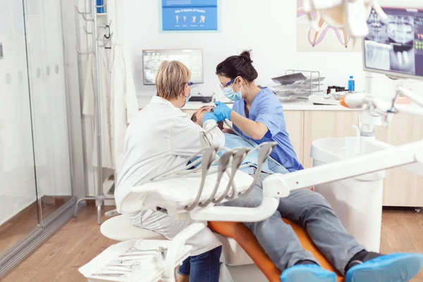 Старшая женщина-стоматолог анализирует зубы больного пациента — стоковое фото