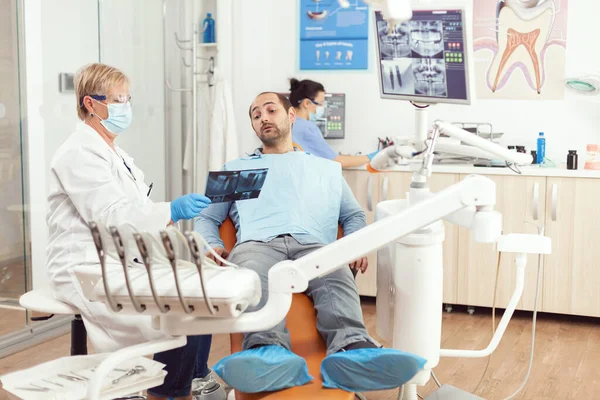 Senior kvinnlig tandläkare behandla sjuk man patient i modern stomatologisk tandvård kontor — Stockfoto