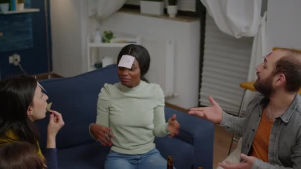 Amici misti di razza con note appiccicose attaccate sulla fronte che giocano indovina chi gioco — Video Stock