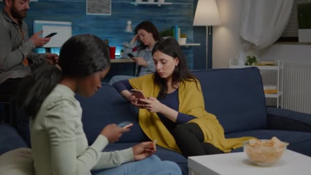 Amis multiraciaux se détendre sur le canapé tout en surfant nouvelles sur Internet en utilisant mobile — Video