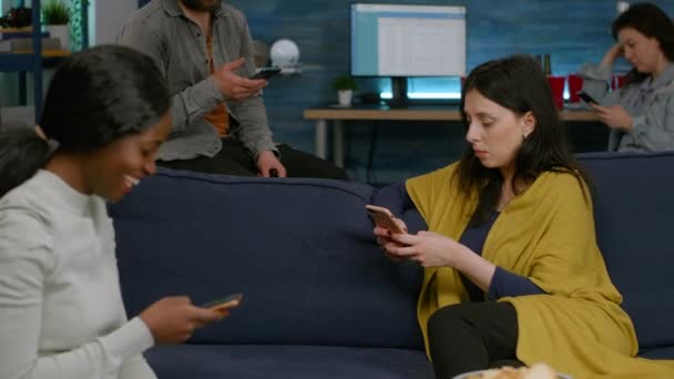 Amici multirazziali seduti sul divano separatamente al telefono navigando su internet — Video Stock