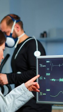 Maskeli kaslı bir sporcu laboratuarda çapraz antrenörle koşuyor.