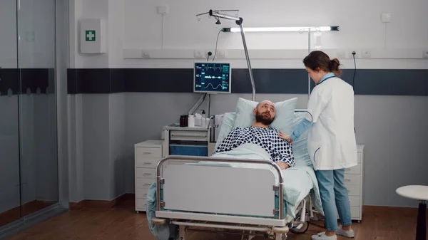 Ο άρρωστος αναπαύεται στο κρεβάτι ενώ ο θεραπευτής παρακολουθεί την αναπνευστική αποκατάσταση — Φωτογραφία Αρχείου