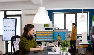 Bilgisayarda çalışan, iki monitörü ve stiliz kalemi olan bir kadın.