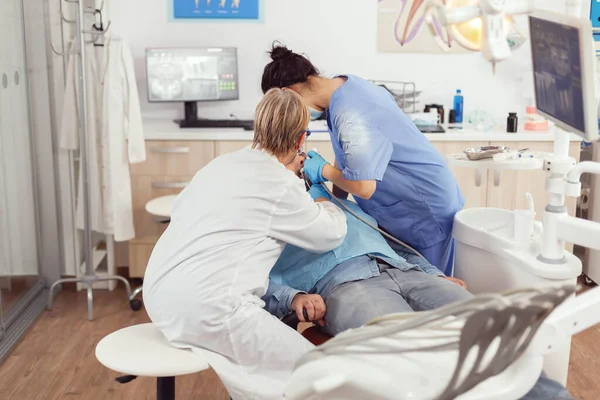 Старшая женщина зубной техник глядя на рот пациента обследования больного человека — стоковое фото
