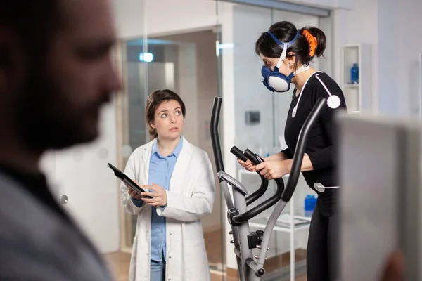 Desportista correndo com máscara em cross trainer com eletrodos ligados — Fotografia de Stock