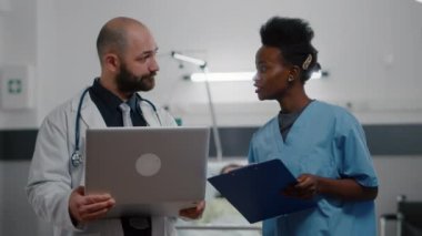 Siyah tenli asistan ve tıp üniformalı pratisyen doktor hastalık belirtilerini izliyor.
