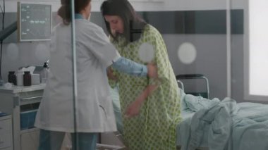 Pratisyen doktorla birlikte zenci asistanı hastanın yataktan kalkmasına yardım ediyor.