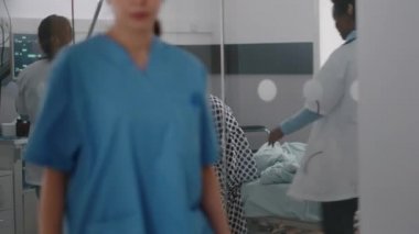 Pratisyen doktorlar hastaya yataktan kalkması için yardım ediyor. Damardan damar içi sıvı torbası tutuyorlar.