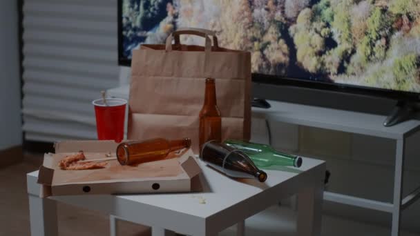Mesa bagunçada com garrafas de cerveja vazias e restos de comida na sala de estar — Vídeo de Stock