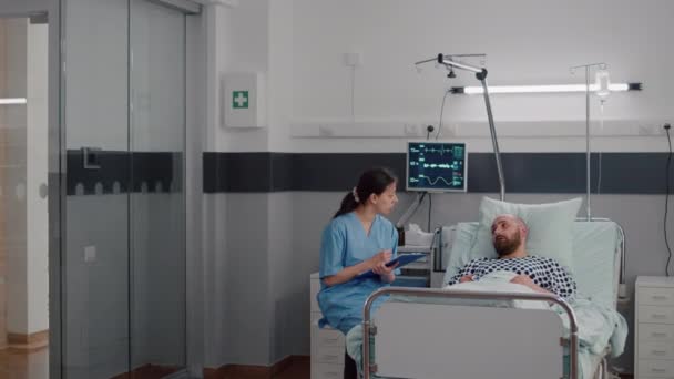 Медична медсестра обговорює лікування хвороби з госпіталізованим хворим чоловіком — стокове відео