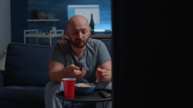 Mutlu genç adam rahat koltukta dinleniyor, patlamış mısır yiyor ve bira içiyor.