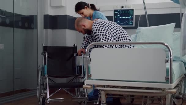 Équipe médicale aidant patient malade avec fracture de jambe mettre en fauteuil roulant — Video