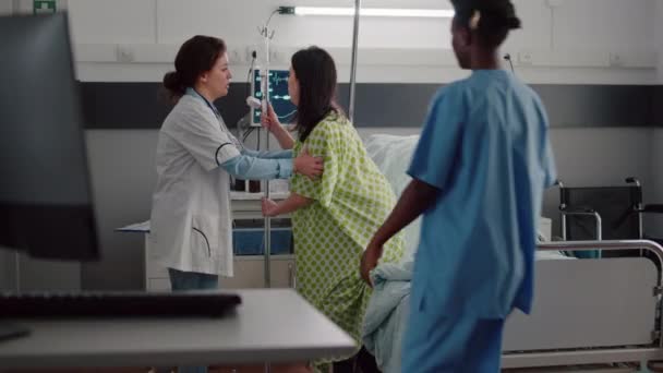 Medical team helping patient to stand up from bed holding intravenous IV fluid drip bag — Stock Video