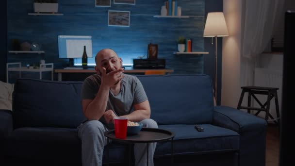 Мужчина наслаждается просмотром сериалов дома, сидя на удобном диване — стоковое видео