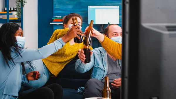 Mixed races people watching tv clinking bottles of beer enjoying time