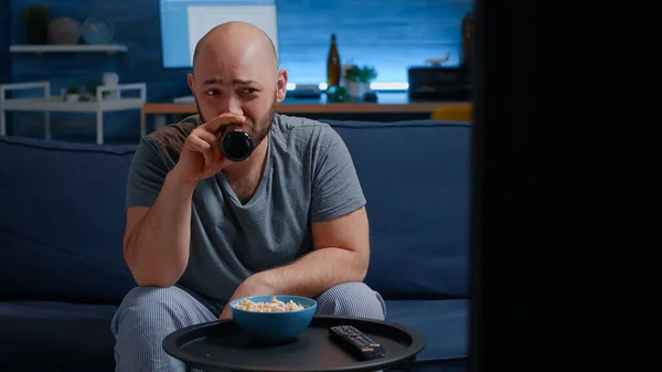 Hombre sentado en un acogedor sofá en la sala de estar solo, comiendo palomitas de maíz, bebiendo cerveza —  Fotos de Stock