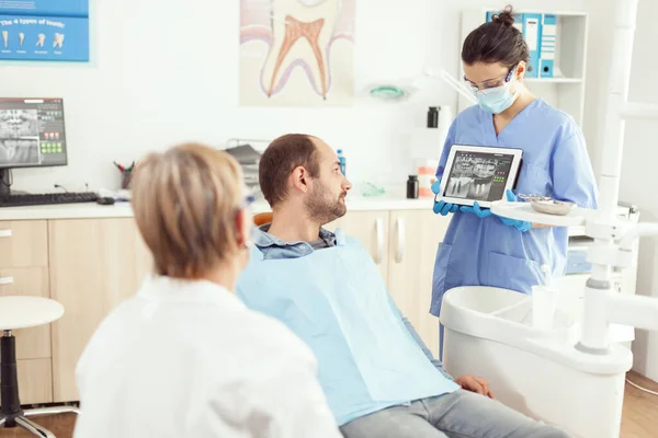 Stomatoloog verpleegkundige in handschoenen met tablet met röntgenfoto van kaak tot zieke patiënt — Stockfoto