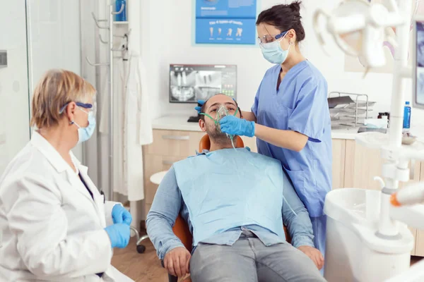 Chory człowiek przygotowuje się do operacji zębów, podczas gdy pielęgniarka zakłada medyczną maskę tlenową — Zdjęcie stockowe